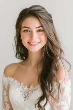 a woman with long hair wearing a white wedding dress and smiling at the camera while standing in front of a gray wall