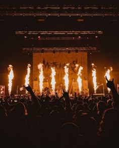 a large crowd at a concert with their hands in the air and flames coming out of them