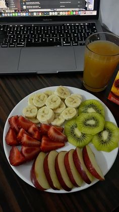 a plate with sliced apples, kiwis and strawberries next to a glass of orange juice