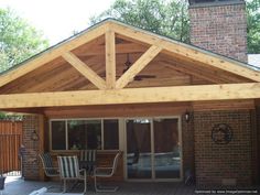 a covered patio with chairs and table on the outside deck area in front of a brick building