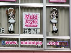 some signs on the side of a building with girls dressed in maid outfits hanging from it's windows