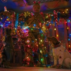 two dogs sit in front of a christmas tree with lights on it and another dog looks at the camera