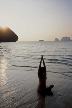 a person sitting in the water on top of a beach next to some rocks and an island