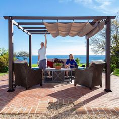 a man and woman sitting at a table under a pergolated gazebo with the ocean in the background
