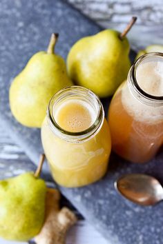 some pears and apples are sitting on a table with spoons next to them
