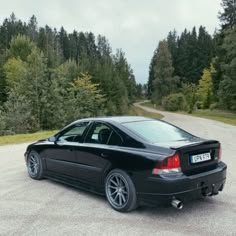 a black car parked on the side of a dirt road next to some trees and grass