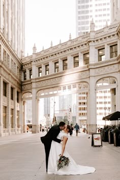 a bride and groom kissing in the middle of an empty street with tall buildings behind them