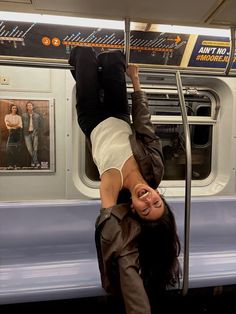 a woman hanging upside down on a subway train with her legs spread out and hands in the air