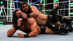 two men wrestling in the middle of a wrestling ring, one is holding another man