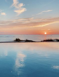 an empty swimming pool with the sun setting over the ocean in the backround