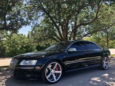 a black car parked in front of a tree on the side of the road with white rims