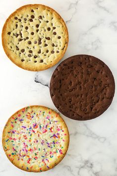three cookies with sprinkles are on a marble countertop next to each other