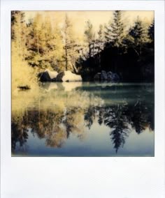 an image of a lake with trees in the background and some rocks on the shore