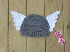 a crocheted hat with white wings on top of a wooden table next to a pink heart