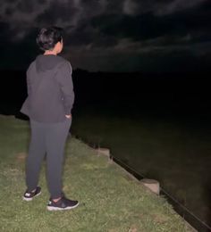 a man standing on top of a lush green field next to a body of water