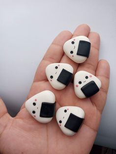 four white and black rocks in the palm of someone's hand, with faces painted on them