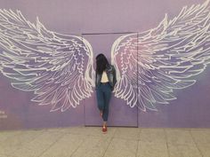 a woman leaning against a purple wall with white wings painted on it's side