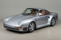 a silver porsche sports car parked in a garage with its door open and the top down