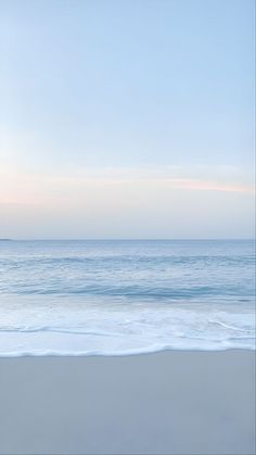 an empty beach with waves coming in to shore and the sky is blue, white and pink
