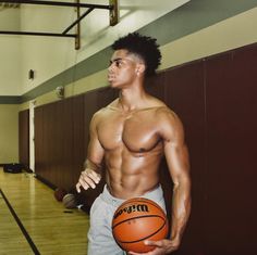 a shirtless man holding a basketball in a gym