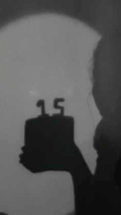 a person holding a cake with the number fifteen on it in front of a dark background