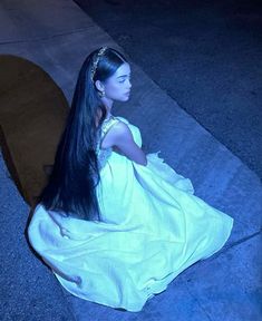 a woman with long black hair sitting on the ground wearing a white dress and headband