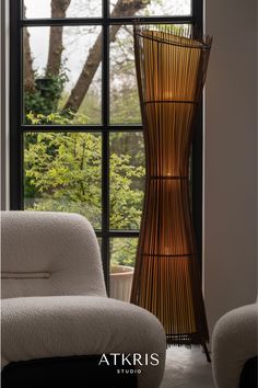 a tall wooden vase sitting next to a window in front of a white couch and chair