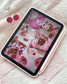 the tablet is sitting on top of the blanket with cherries around it and an apple next to it
