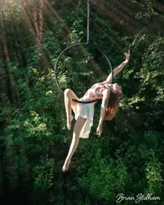 a woman is hanging upside down in the air with a hoop above her head and trees behind her