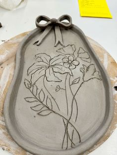 a clay plate with flowers on it sitting on a table next to some paper and scissors
