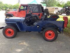 an old blue jeep with red wheels parked in a parking lot
