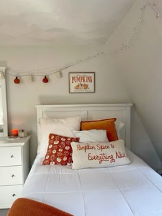 a white bed topped with lots of pillows next to a night stand and dressers