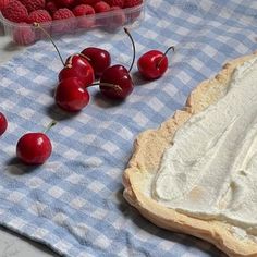 fresh cherries and whipped cream on a blue checkered cloth next to a container of raspberries