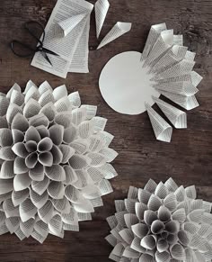 three paper flowers and scissors on a table with some cut out pieces of paper next to them