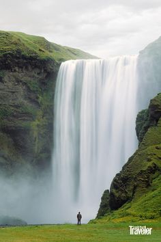 a man standing at the base of a tall waterfall with water cascading over it