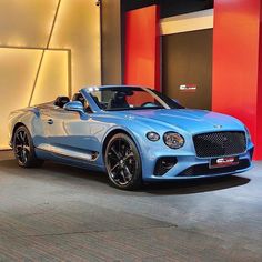 a blue sports car parked in front of a red and white wall with the door open