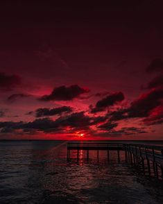 the sun is setting over the ocean with a pier in the foreground and clouds in the background