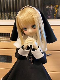 a doll with blonde hair wearing a nun outfit and holding a cross in her hands