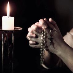 a person holding a rosary in front of a lit candle with their hands on it