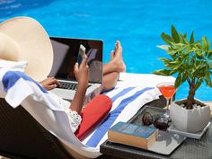 a woman laying on top of a chair next to a pool using a laptop computer