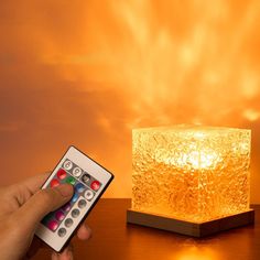 a person is holding a remote control in front of a glowing light cube on a table