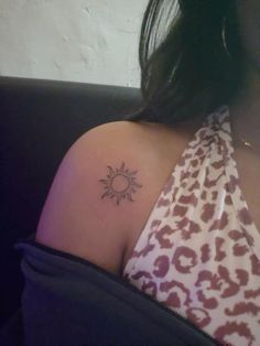a woman with a small sun tattoo on her upper arm and shoulder, sitting in a chair
