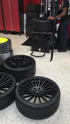 four black rims and tires on the floor in front of a tire changer