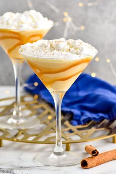 two martini glasses filled with whipped cream and cinnamon on a gold platter next to an orange napkin