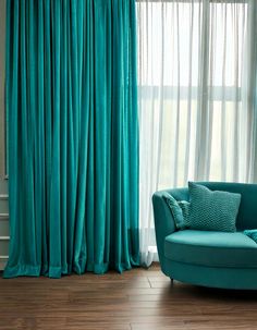a blue couch sitting in front of a window with curtains on the windowsills