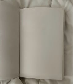an open book sitting on top of a white sheet covered bed next to two pillows