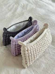 three crocheted purses sitting on top of a white bed covered in sheets