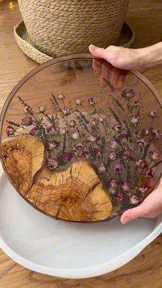 a person holding a plate with flowers in it on a table next to a potted plant