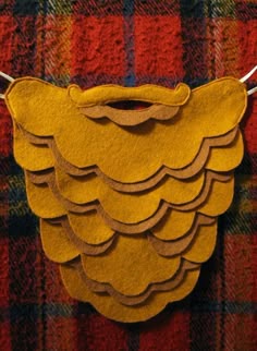 a yellow piece of felt hanging from a string on a plaid cloth wall with red and green flannel
