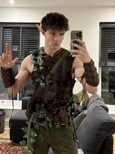 a young man dressed in costume taking a selfie with his cell phone while standing in the living room